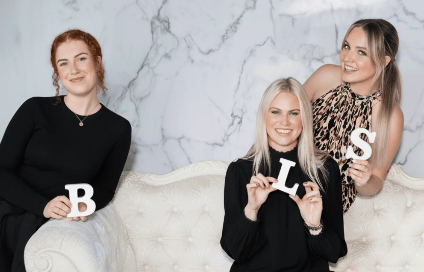 Beauty Lounge St Kilda team with the B·L·S letters on the cream Victorian chaise